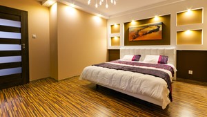 fotografía de habitación amoblada, varias fuentes de luz y cama tamaño grande, con parquets de madera clara